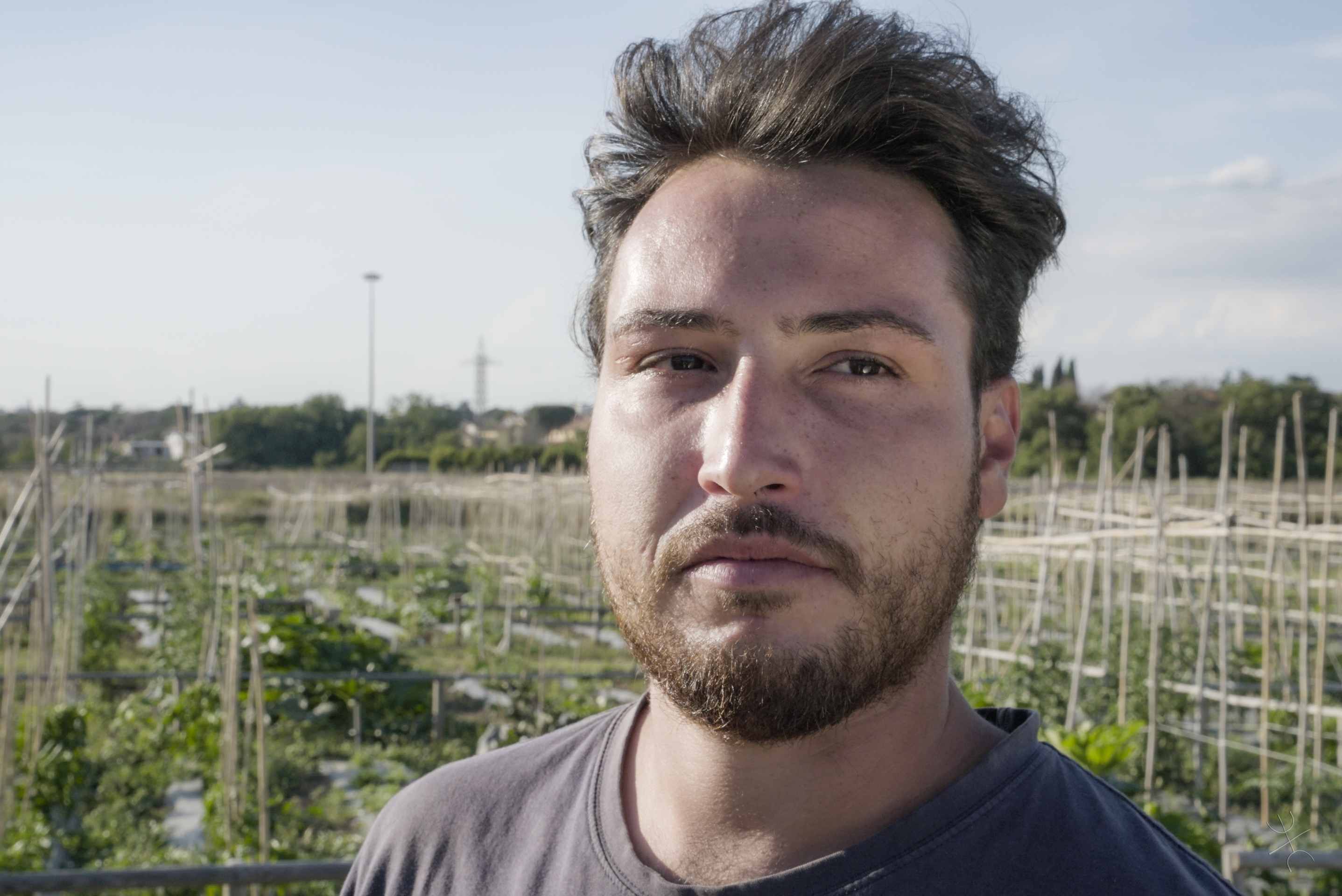 agricoltore con barba con alle spalle un orto