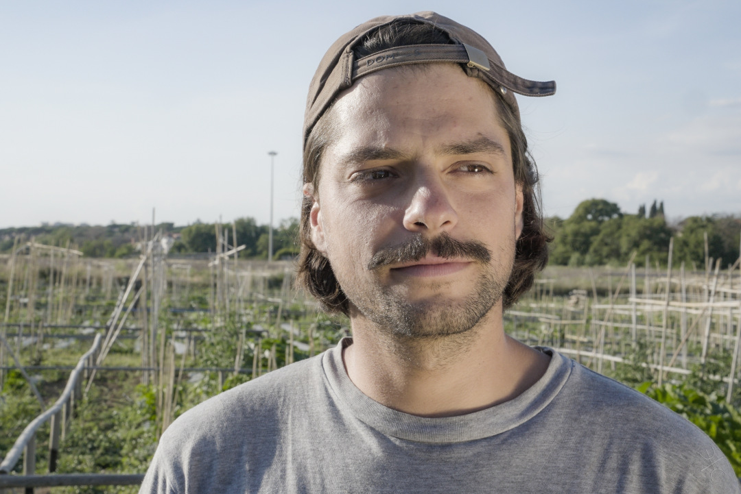 agricoltore con baffi e cappello con alle spalle un orto